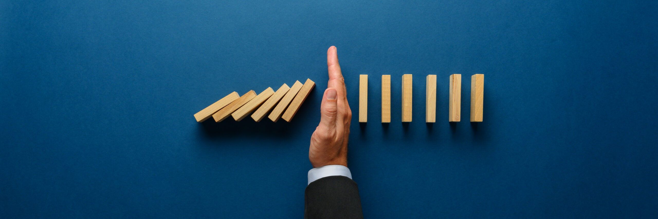 A person in a suit prevents dominoes from falling by holding up wooden blocks. 1