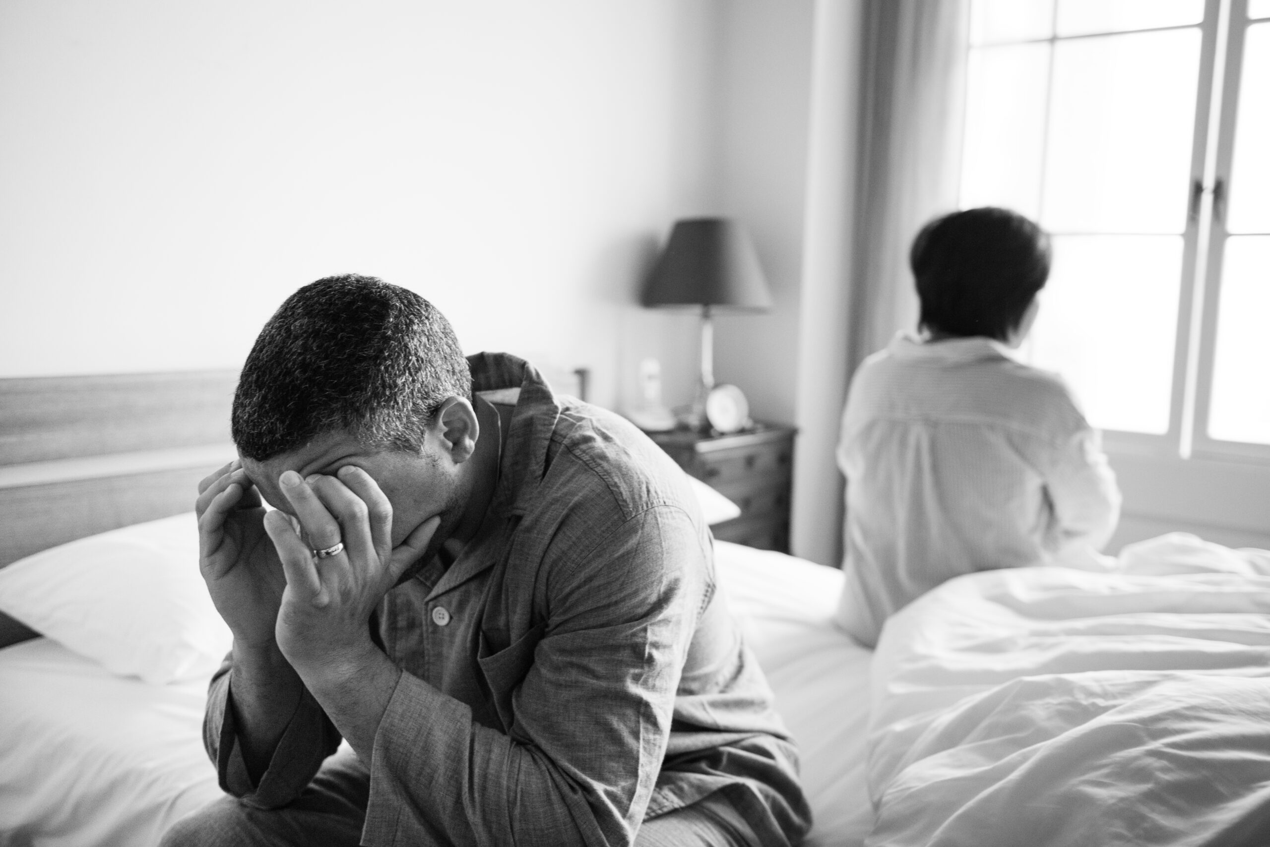 Man and woman contemplating life's drama on a bed by the window.